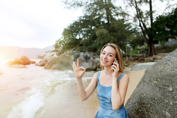 Foto de luz ensolarada da menina mostrando ok e sentado na praia, falando por smartphone Hawaii . — Fotografia de Stock