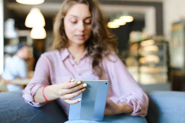 Chica encantadora joven sentada en el sofá en la cafetería y el uso de la tableta . — Foto de Stock