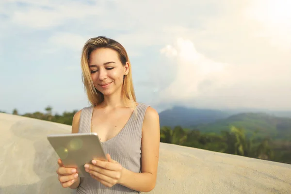 Young smiling woman using tablet with mountains background, Thailand.
