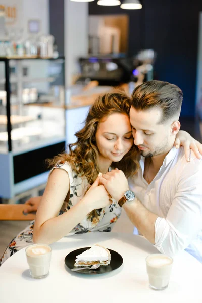 Junges nettes Paar sitzt mit Kaffee, Kuchen und Umarmungen im Café. — Stockfoto