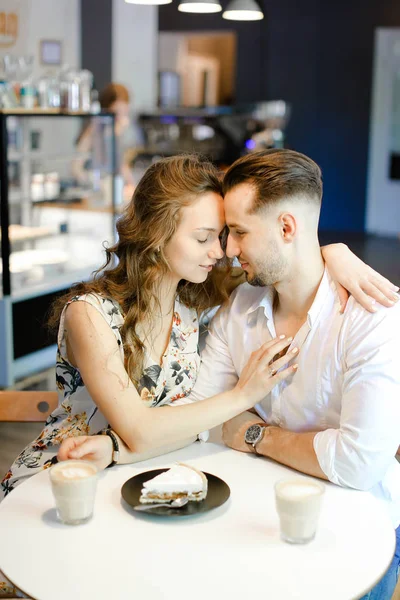 Junges kaukasisches Paar sitzt mit Kaffee, Kuchen und Umarmungen im Café. — Stockfoto