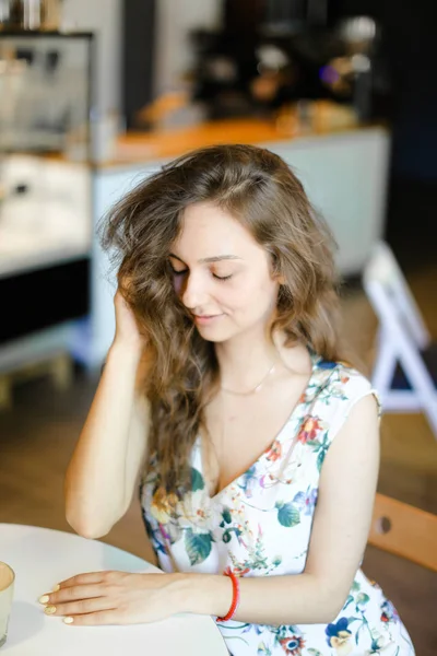 Młoda cute kobieta siedzi w kawiarni i dotykając kręcone włosy. — Zdjęcie stockowe