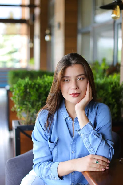 Mulher caucasiana sentada no café apoiada na mão, vestindo camisa jeans — Fotografia de Stock