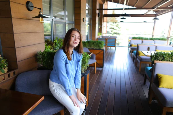 Kvinna sitter i fåtölj på Café nära rumsväxter och bord. — Stockfoto