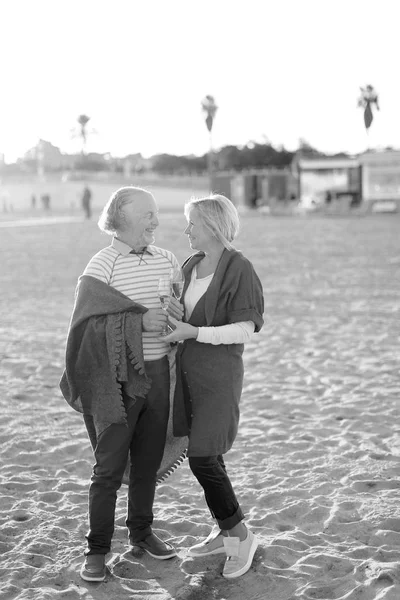 Czarno-białe zdjęcie dwóch emerytów stojący na piaszczystej plaży z kieliszków szampana. — Zdjęcie stockowe