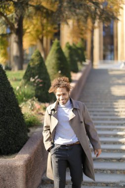 Afro amerikan gülümseyen çocuk parkta çalılar yanında beton merdivenlerde ayakta.