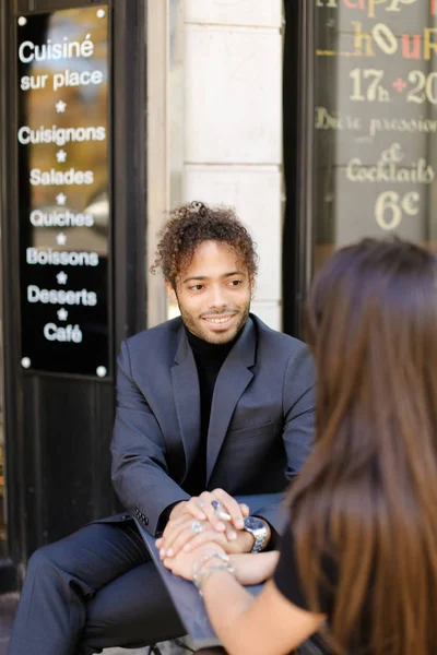 Concéntrese en el hombre afroamericano sosteniendo las manos femeninas y sentado en la cafetería de la calle . — Foto de Stock
