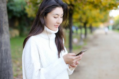 Kore kız Smartphone kullanarak ve parkta yürüyüş.