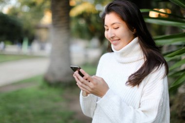 Akıllı telefon kullanan ve tropikal parkta yürüyen Çinli kız..