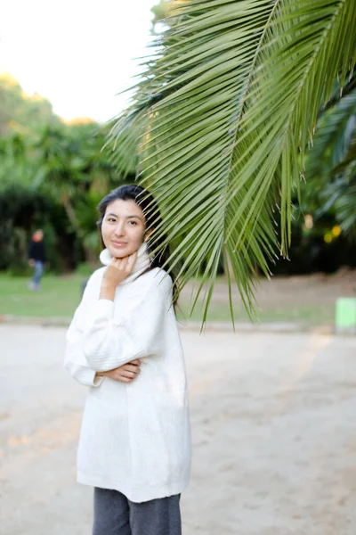 Koreansk söt flicka i vit tröja står nära palmblad. — Stockfoto