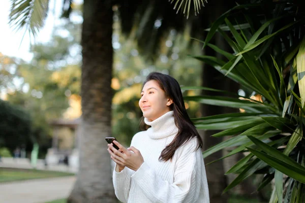 Chica china usando teléfono inteligente y caminando en el parque tropical . — Foto de Stock