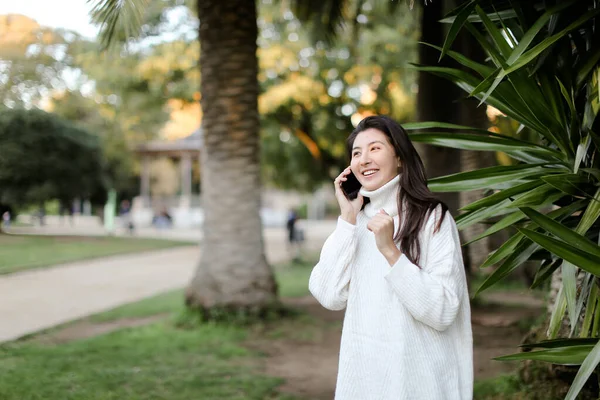 Chica coreana en el parque tropical hablando por teléfono inteligente cerca de la palma . — Foto de Stock