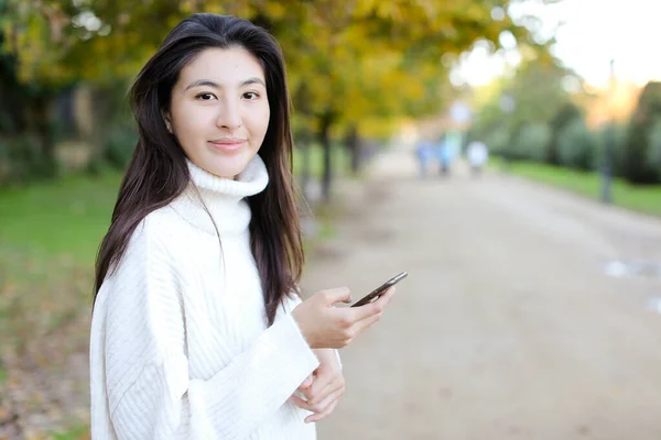 Japonská dívka pomocí smartphone a chůze v parku. — Stock fotografie