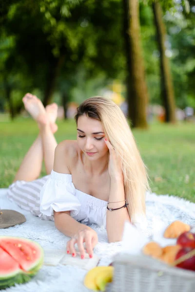 Young woman lying on plaid in park and reading book. — Stockfoto