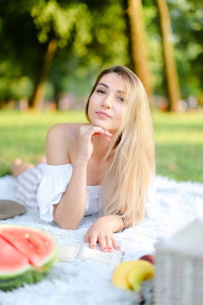 Young blonde girl lying on plaid in park and reading book. — Stock Photo, Image