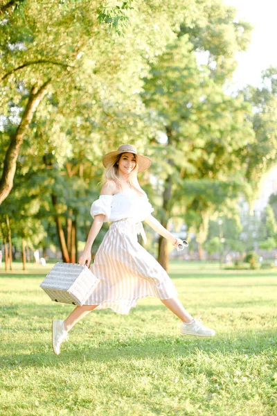 Ung kvinna hoppar i parken och kör, bär fashionabla kläder och hatt. — Stockfoto