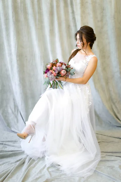 Foto pengantin muda duduk di studio dengan karangan bunga . — Stok Foto