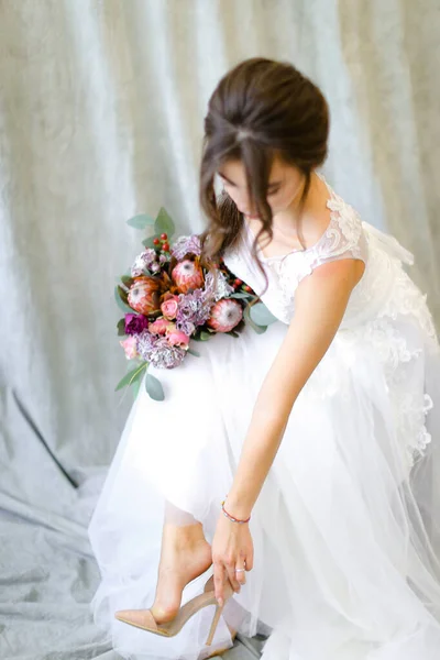 Νεαρή νύφη με λουλούδια που φοράει παπούτσια στο φωτογραφείο. — Φωτογραφία Αρχείου