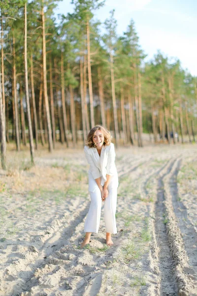 Bionda bella donna che cammina sulla spiaggia di sabbia e indossa vestiti bianchi . — Foto Stock