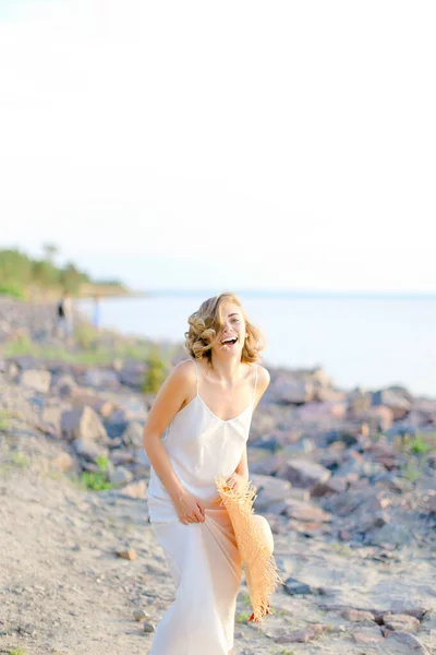 Mulher muito sorridente andando na praia rochosa com hant nas mãos e vestindo vestido . — Fotografia de Stock