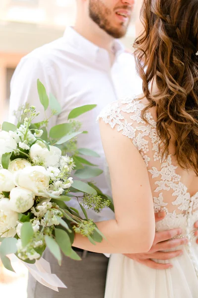Noivo europeu feliz beijando noiva mantendo buquê de flores . — Fotografia de Stock