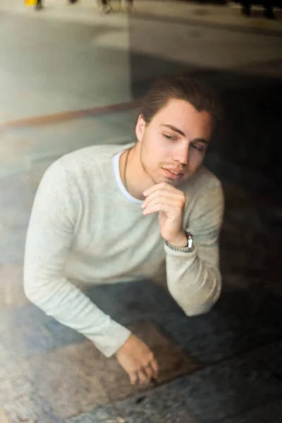 Fiatal ember ül, elmélkedés ablakban viselése szürke pulóver. — Stock Fotó