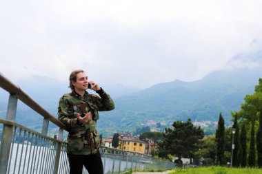 Avrupa delikanlı yanında tırabzan, Como Gölü ve Alpler Dağı arka planda smartphone konuşuyor.