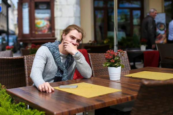 Joven hombre de negocios sentado en la cafetería de la calle y usando suéter gris . — Foto de Stock