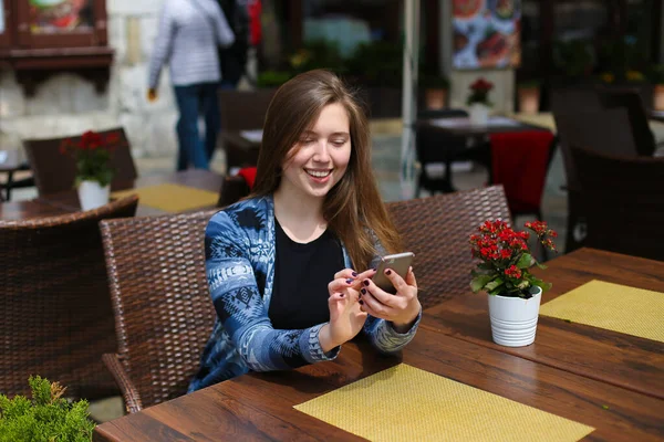 Young caucasian female person typing message by smartphone at cafe near red flowers. — Stock Photo, Image