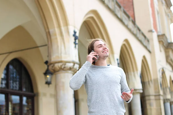 Young male person talking by smartphone near building with columns in background.