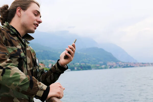 Joven hombre guapo usando teléfono inteligente cerca del lago Como y la montaña de los Alpes en el fondo . — Foto de Stock