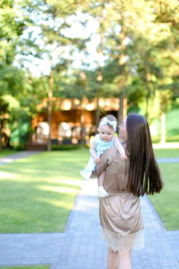 Esmer kadın kişinin bahçede küçük bebek tutan arkadan görünüm.