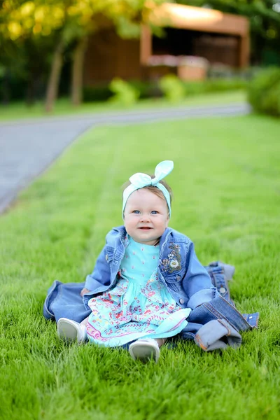 Niña sentada sobre hierba verde y con chaqueta vaquera . — Foto de Stock