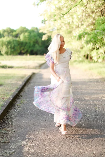 Giovane donna bionda vestita di bianco che cammina fuori vicino all'albero in fiore . — Foto Stock