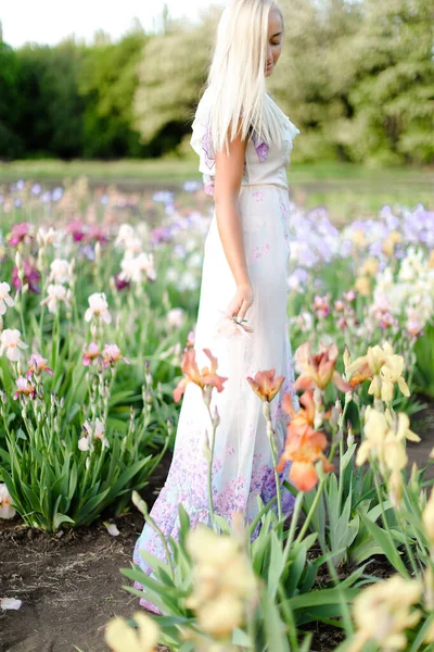 Menina jovem vestindo vestido branco de pé perto íris no jardim . — Fotografia de Stock