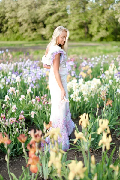 Młoda dziewczyna europejskiej noszenie białej sukni stojącej w pobliżu irysy na ogród. — Zdjęcie stockowe