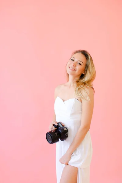 Jovem fotógrafa sorridente com câmera em fundo monofônico rosa . — Fotografia de Stock