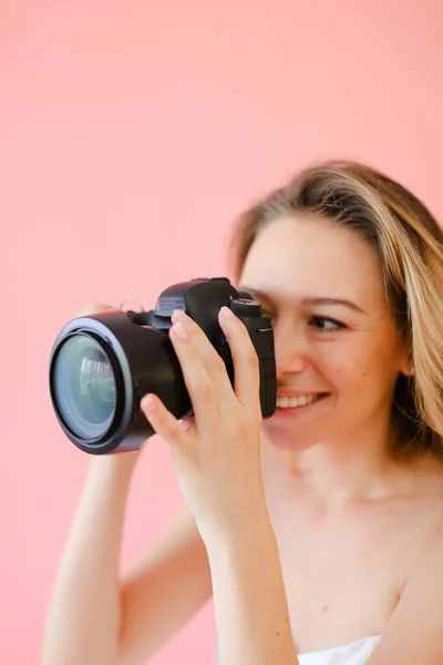 Närbild ung kvinnlig fotograf med kamera i rosa monofoniska bakgrund. — Stockfoto