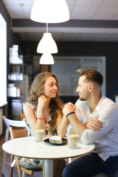 Junges hübsches Mädchen und Junge sitzen im Café in der Nähe von leckerem Kuchen und halten Händchen. — Stockfoto