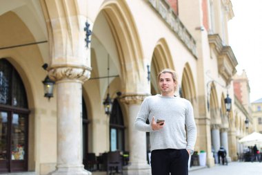 Arka planda sütunlarla building yakınındaki smartphone ile yürüyen Genç beyaz adam.