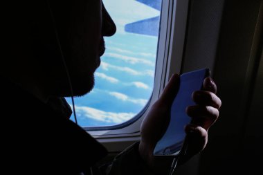Uçak penceresinde yakınındaki smartphone kullanarak sakallı adam silüeti portre.