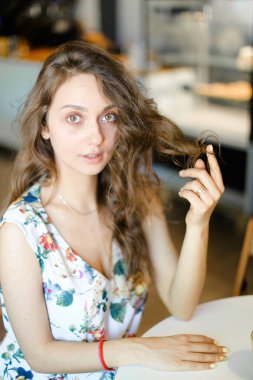 Kafede oturan ve kıvırcık saç dokunmadan genç güzel öğrenci.