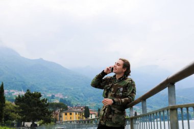 Yakışıklı delikanlı yanında tırabzan, Como Gölü ve Alpler Dağı arka planda smartphone konuşuyor.