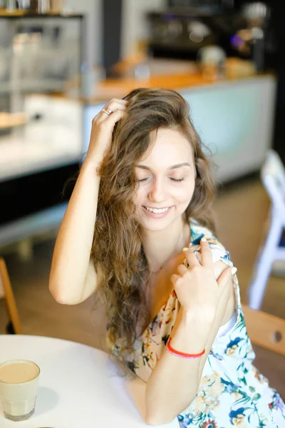 Młoda kobieta uśmiechający się siedząc w kawiarni i dotykając włosów kręconych. — Zdjęcie stockowe