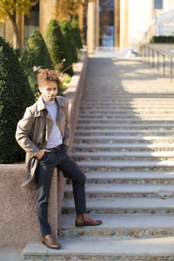 Afro-Amerikalı genç çocuk parktaki çalıların yanında beton merdivenlerde duruyor..