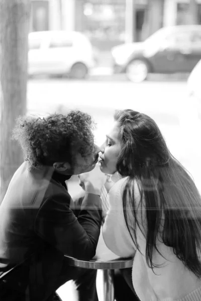 Black and white photo of afro american man kissing caucasian girl, reflection in glass.