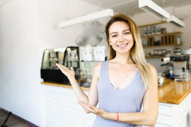 Sarışın kafe yöneticisi ayakta ve gülümsüyor..