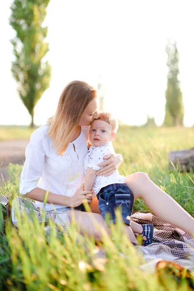 Giovane madre bionda baciare bambino su plaid, erba su sfondo . — Foto Stock