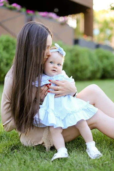 Młoda matka z długimi włosami, siedząc na trawie z córeczką. — Zdjęcie stockowe