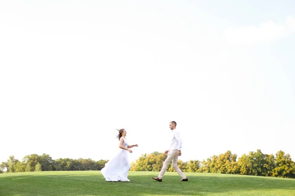 Glad brud och brudgum som springer till varandra på gräs i vit himmel bakgrund. — Stockfoto